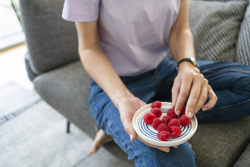 Hands of woman holding fresh raspberries in plate - SVKF00877