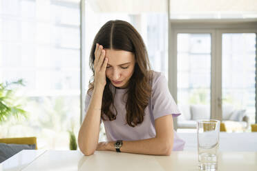 Stressed woman with head in hand leaning on table at home - SVKF00885