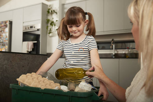 Mother with daughter holding recycling bin at home - PMF02398