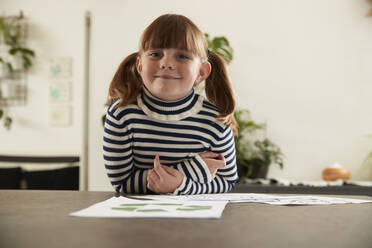 Lächelndes Mädchen mit Papieren, die auf einem Tisch zu Hause liegen - PMF02408