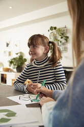 Happy girl with sister coloring recycling symbol with pen at home - PMF02411