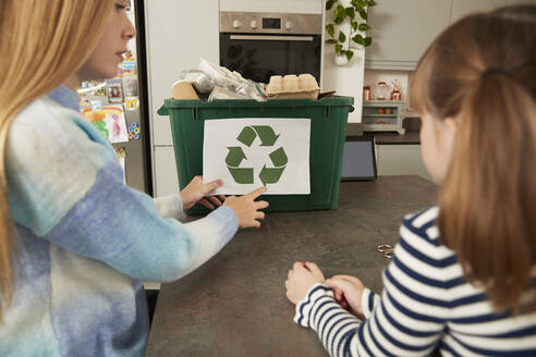 Mädchen mit Schwester klebt Symbol auf Mülleimer zu Hause - PMF02415