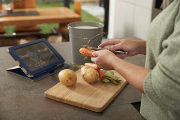 Woman with tablet PC peeling carrot preparing meal at home - PMF02420