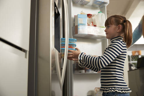 Mädchen bewahrt Plastikbehälter im Kühlschrank zu Hause auf - PMF02438