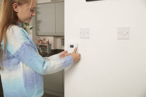 Lächelndes Mädchen beim Einstellen des Thermostats an der Wand zu Hause - PMF02442