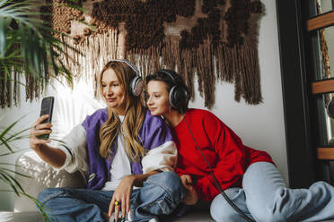 Smiling musician with colleague taking selfie through mobile phone on sofa in studio - MDOF00328