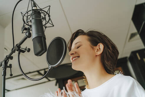 Smiling singer recording music through microphone in studio - MDOF00336