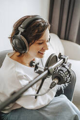 Happy musician recording podcast through microphone in studio - MDOF00341