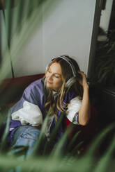 Smiling woman wearing headphones on sofa in recording studio - MDOF00344