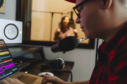 Toningenieur komponiert am Laptop mit Sängerin im Hintergrund im Aufnahmestudio - MDOF00356