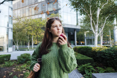 Nachdenkliche junge Frau isst Apfel vor einem Gebäude - ASGF03133