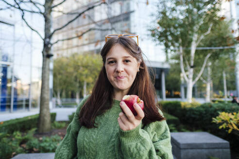 Lächelnde Frau mit Apfel vor einem Gebäude - ASGF03135