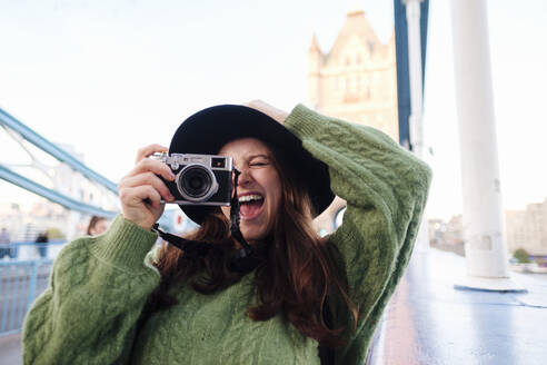 Glückliche junge Frau, die durch die Kamera auf der Tower Bridge, London, England, fotografiert - ASGF03141