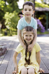 Lächelnder Junge mit Schwester im Garten sitzend - ONAF00307