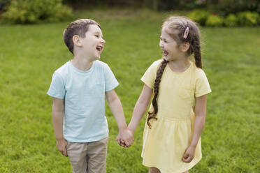 Brother and sister holding hands and laughing together in back yard - ONAF00314