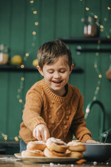 Glücklicher Junge mit Zimtschnecken in der Küche - VSNF00169
