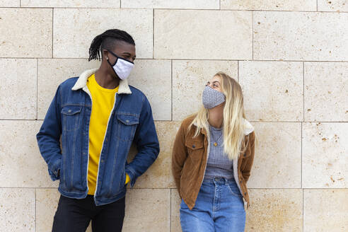 Young friends wearing protective face masks in front of wall - JPTF01141