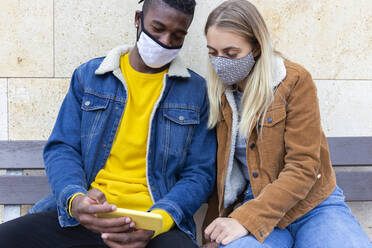 Woman with man using smart phone sitting on bench - JPTF01143