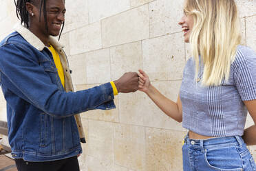 Friends giving fist bump together standing in front of wall - JPTF01150