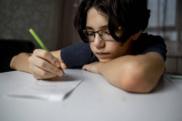 Junge schreibt mit Stift auf Papier zu Hause - ANAF00640