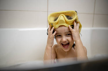 Glücklicher Junge mit Schwimmbrille beim Baden im Badezimmer zu Hause - ANAF00645