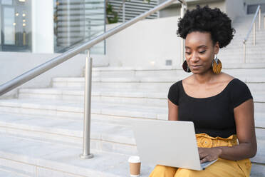 Smiling freelancer working on laptop sitting on steps - SVKF00928