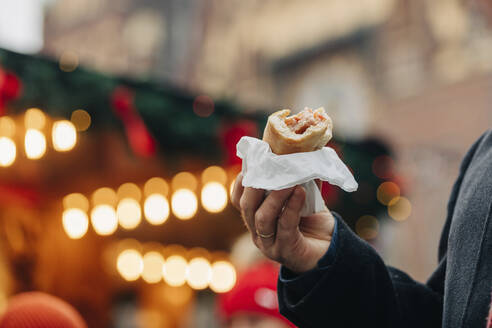 Hand eines Mannes mit Hot Dog auf dem Weihnachtsmarkt - VSNF00196