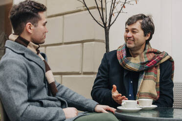 Glücklicher Vater und Sohn sitzen mit Kaffeetassen in einem Straßencafé - VSNF00201