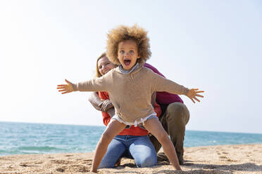 Screaming girl standing with arms outstretched in front of mother and father at beach - MEGF00297