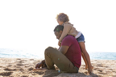 Mädchen umarmt Vater am Strand sitzend an einem sonnigen Tag - MEGF00301