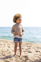 Nettes Mädchen mit Afrofrisur steht vor dem Meer am Strand - MEGF00302