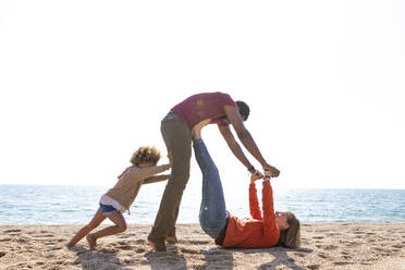 Glückliche Frau spielt mit Mann und Tochter am Strand - MEGF00303