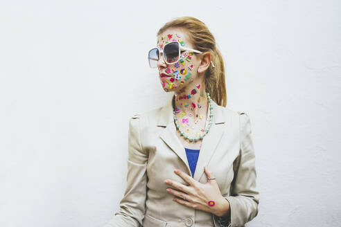 Frau mit bunten Aufklebern im Gesicht und Sonnenbrille vor weißem Hintergrund - SVCF00232