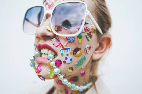 Woman with multi colored stickers on face biting necklace in front of white background - SVCF00237