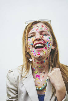 Glückliche Frau mit mehrfarbigen Aufklebern im Gesicht auf weißem Hintergrund - SVCF00248