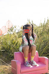 Girl photographing though toy camera sitting on pink armchair - MEGF00322