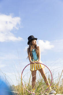 Girl wearing hat holding plastic hoop on grass - MEGF00332