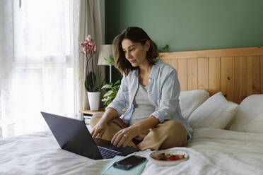 Pregnant businesswoman using laptop on bed at home - TYF00500