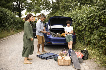 Family discussing with each other looking at picnic supplies while standing near car - MASF33446