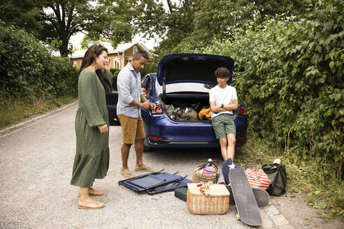 Familie diskutiert miteinander, während sie in der Nähe des Autos steht und sich Picknickzubehör ansieht - MASF33446