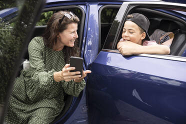 Glückliche Mutter zeigt ihrem Sohn im Auto sitzend das Smartphone - MASF33452