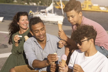 Familie genießt Eis miteinander, während sie auf einer Bank sitzen - MASF33469