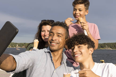 Glücklicher Mann, der ein Selfie mit seiner Familie über sein Smartphone macht, während er im Urlaub ein Eis isst - MASF33472