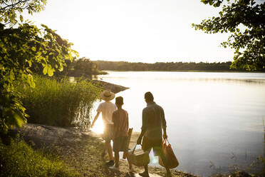 Family with picnic supplies walking at lakeshore during summer vacation - MASF33480