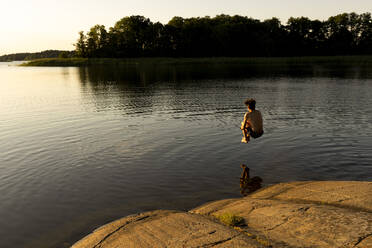 Junge springt im Urlaub bei Sonnenuntergang in den See - MASF33489