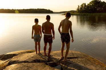 Rear view of father with sons standing on rock at sunset during vacation - MASF33490