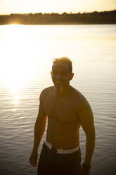 Glücklicher Mann ohne Hemd am See bei Sonnenuntergang - MASF33493