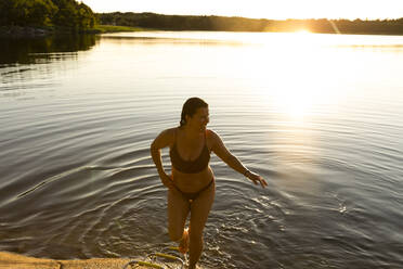 Happy woman in bikini walking out of lake after swimming during sunset stock  photo