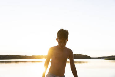 Shirtless boy looking down against clear sky on sunset - MASF33508