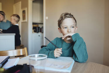 Nachdenklicher Junge mit Bleistift und Buch am Tisch sitzend - MASF33515